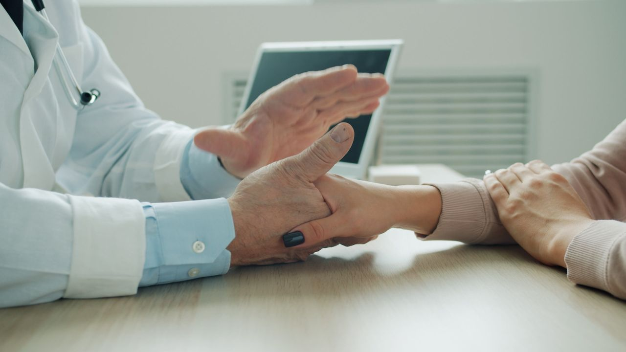 Close-up of a doctor holding a patient's wrist during a consultation in a medical office.